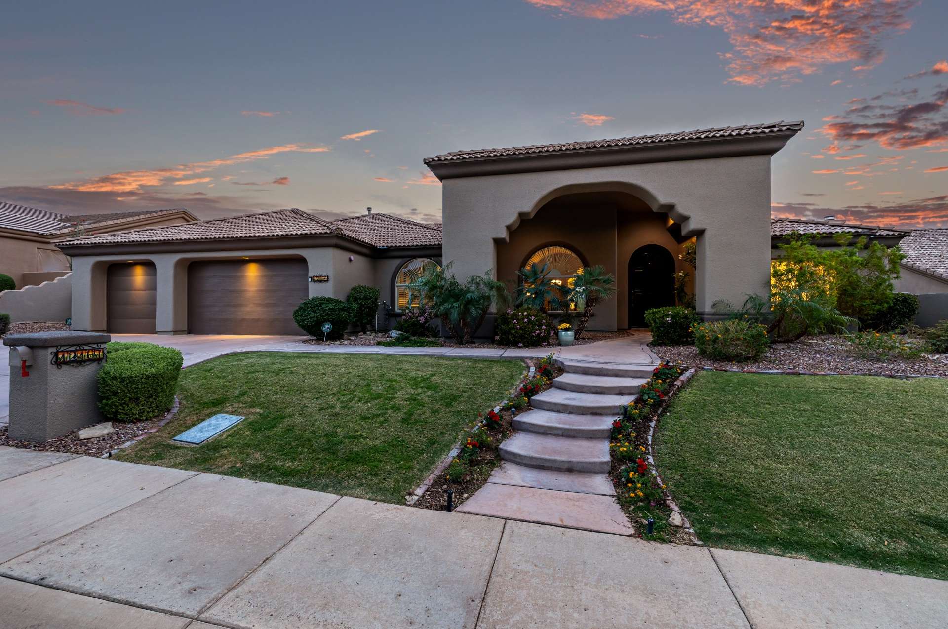60 of 65. Follow the flower-lined walkway to an elegant arched entrance framed by tropical plants and desert-friendly landscaping. A picture-perfect front yard ready to welcome guests in style.