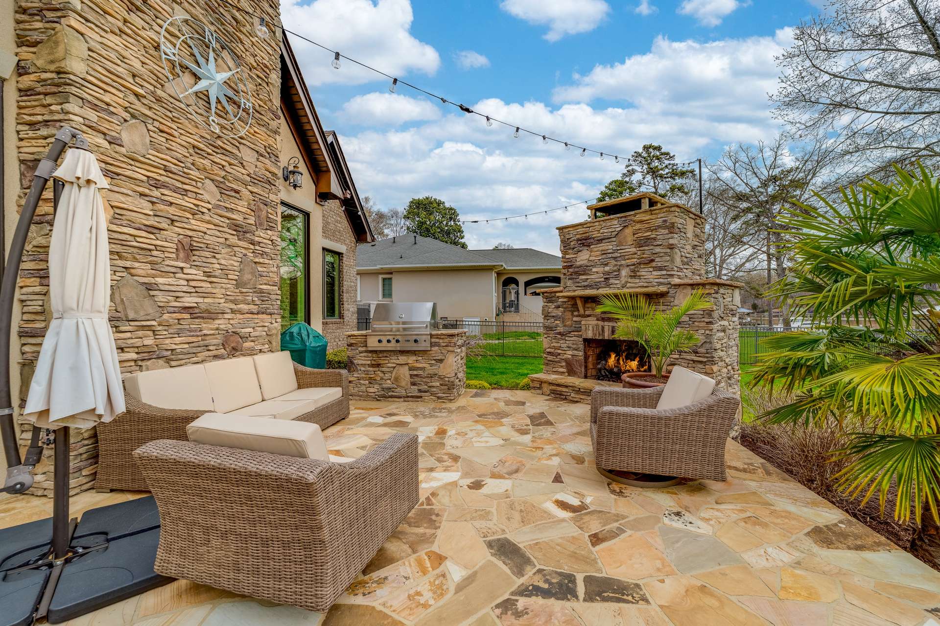 52 of 79. Exterior Day Time Photo - 846 Armstrong Rd - Showcasing Back Patio, featuring a stacked stone wood burning fireplace, built in Viking Grille overlooking backyard and lake