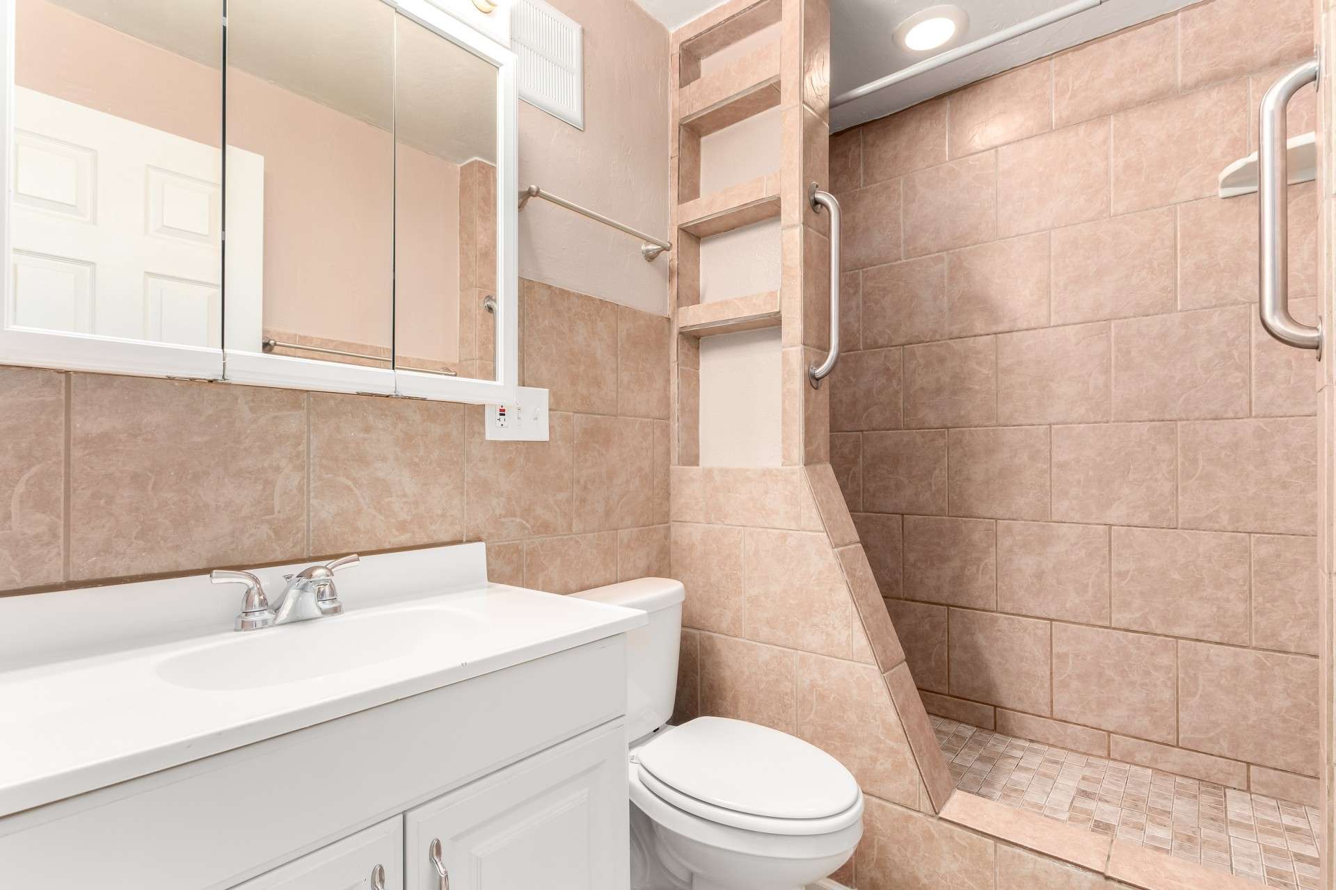 20 of 26. The sleek bathroom design features a walk-in tiled shower with built-in shelving and grab bars, ensuring both modern appeal and accessibility. A well-lit vanity and ample storage make this bathroom both functional and elegant in a desirable Phoenix location.