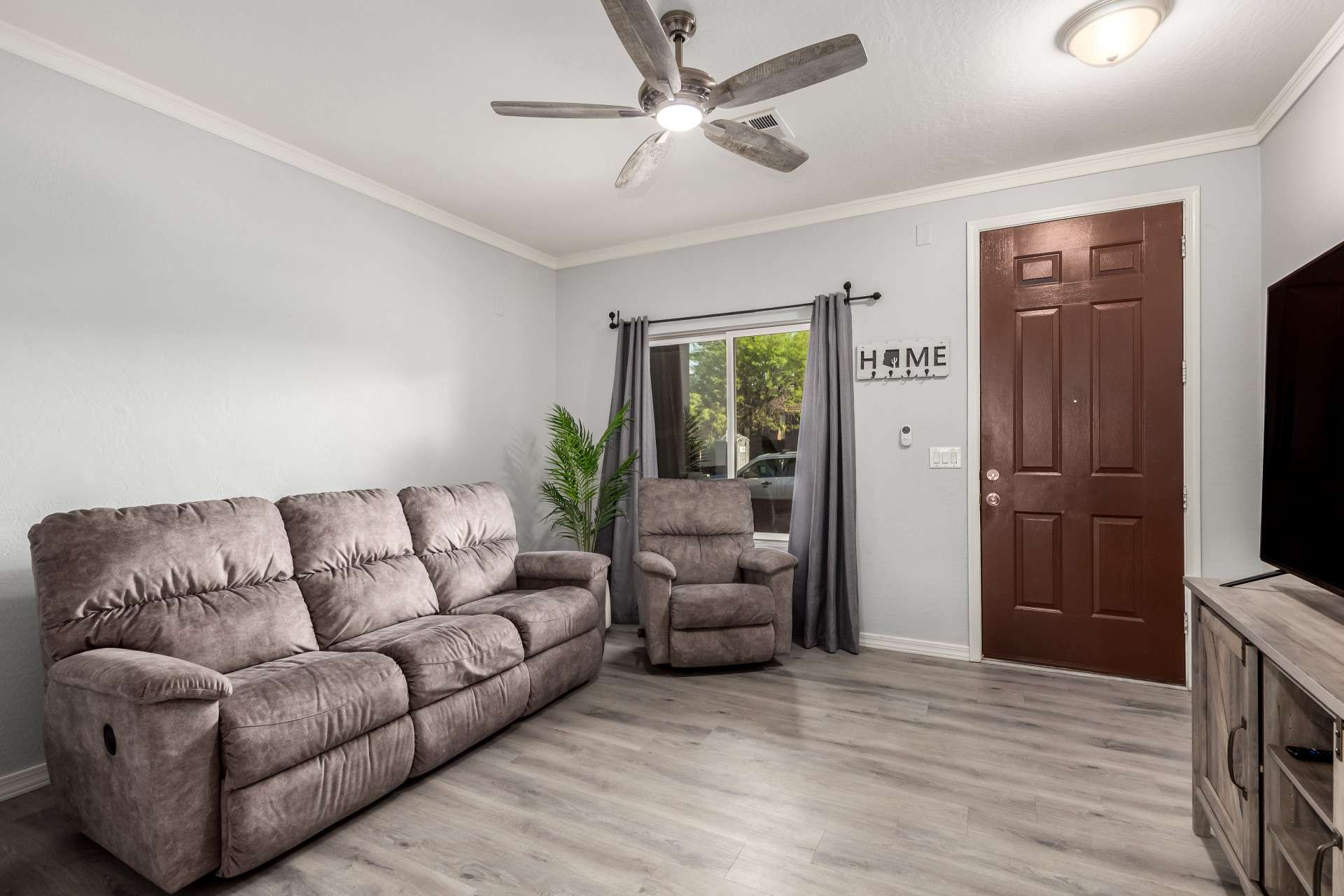 5 of 37. The front living area features crown molding, soft gray walls, and wood-look flooring for a cozy yet contemporary feel. Natural light fills the space, creating a welcoming entry for guests.