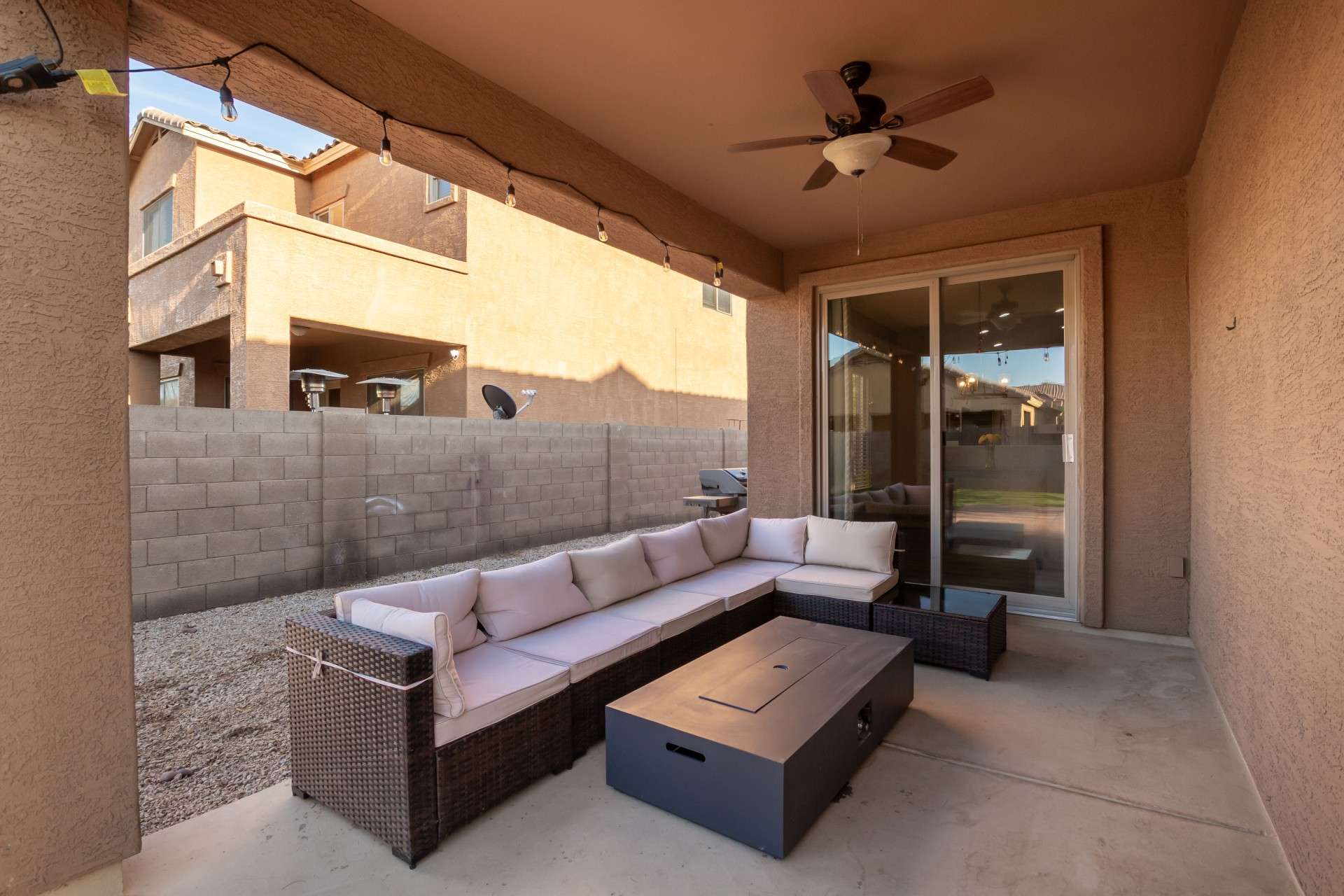 28 of 37. Enjoy Arizona evenings in this shaded covered patio featuring a ceiling fan, warm stucco finishes, and a cozy sectional setup. Perfect for relaxing or entertaining, the space opens seamlessly to the backyard through sliding glass doors.