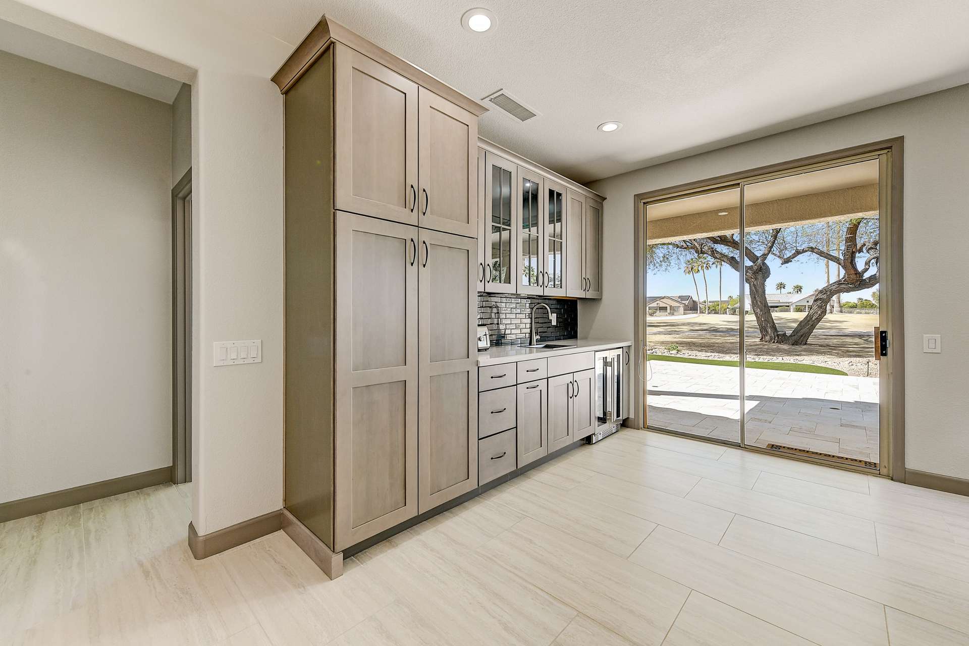 9 of 35. This bonus kitchen space features extensive cabinetry with glass uppers, a built-in wine fridge, and a wet bar ideal for entertaining. Premium finishes and direct patio access make this area both practical and luxurious.