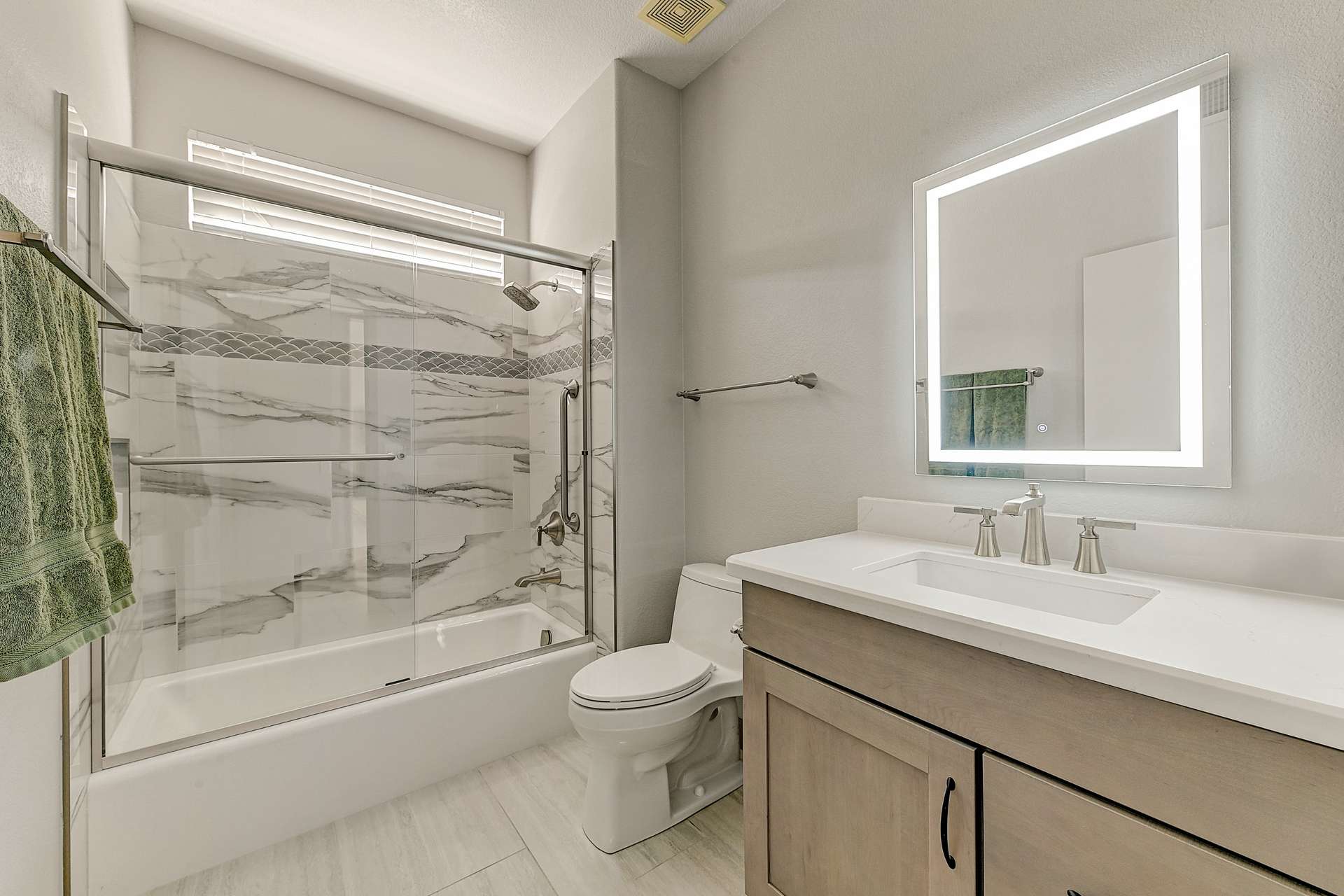 24 of 35. This updated guest bathroom features a quartz vanity, backlit LED mirror, and a designer tile tub/shower combo. Stylish and functional for everyday comfort.