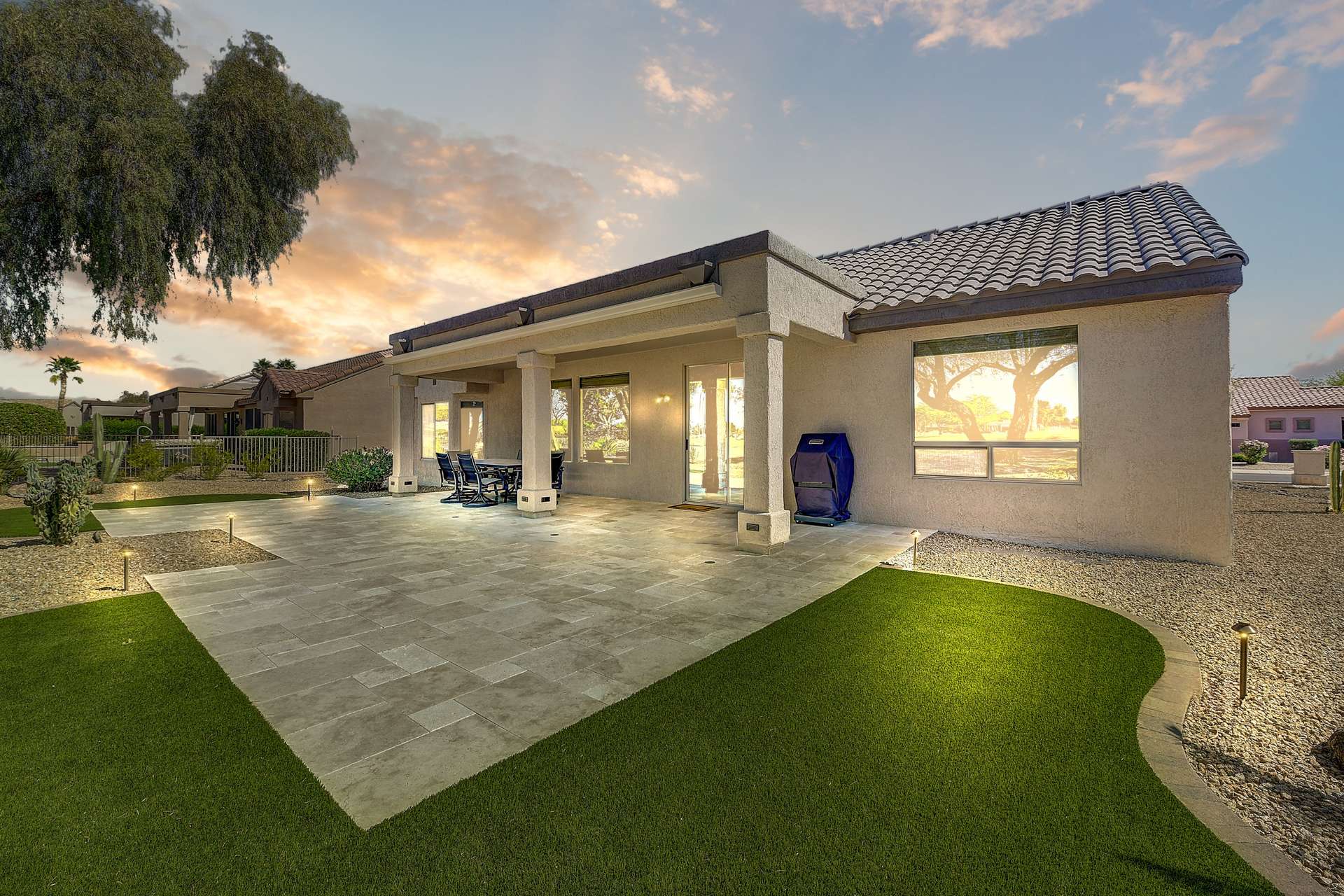 32 of 35. This spacious backyard features an extended travertine patio with artificial turf accents, perfect for outdoor entertaining. Evening lighting enhances the luxurious yet low-maintenance design.