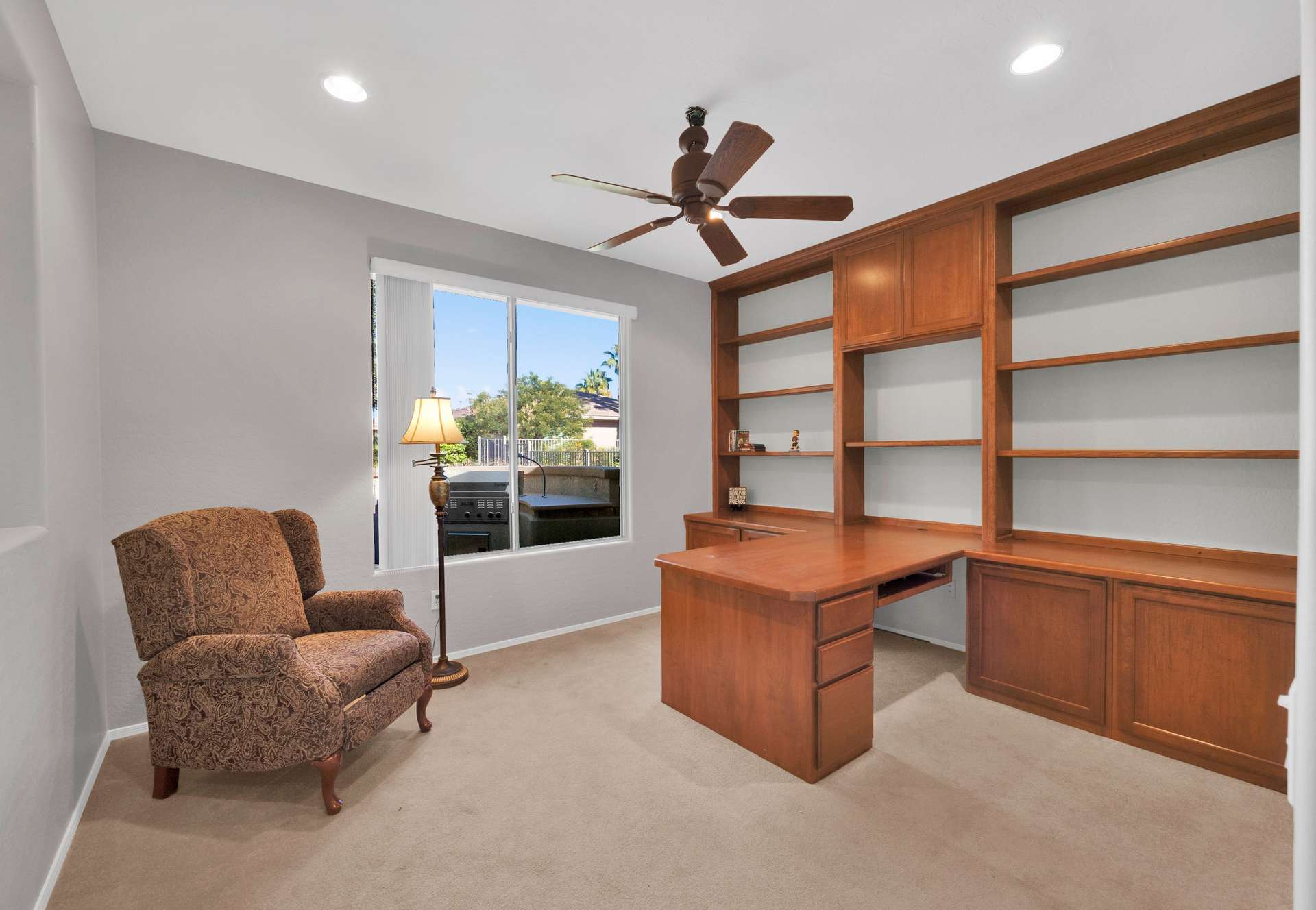 11 of 13. Enjoy productivity and comfort in this sunny home office featuring built-in shelving, a spacious wraparound desk, and a large window with serene backyard views perfect for remote work or reading in this Surprise AZ rental.