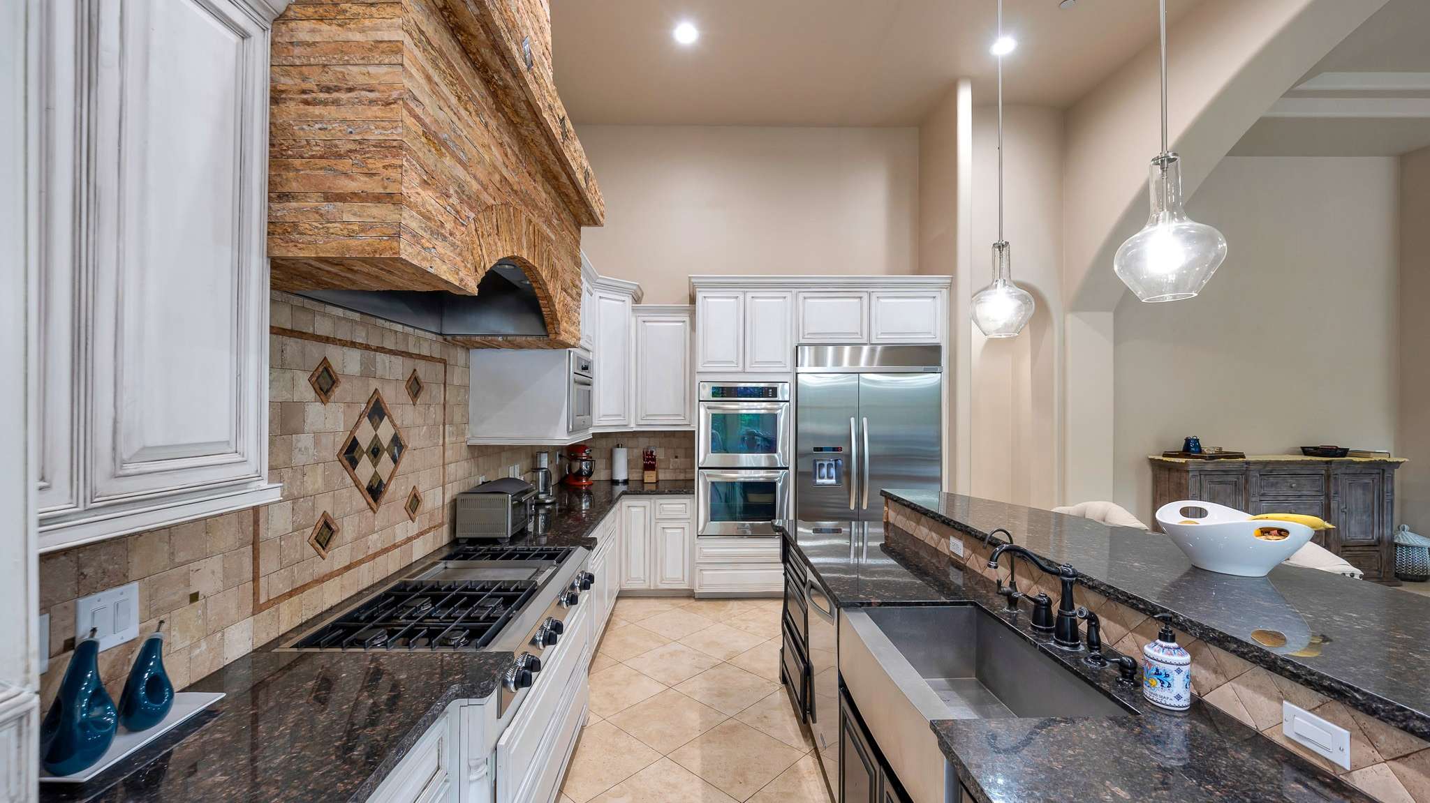 12 of 39. A standout kitchen featuring stainless appliances, double ovens, granite counters, and a dramatic stone range hood. Ample cabinetry and an oversized island complete this Scottsdale chef s dream setup.