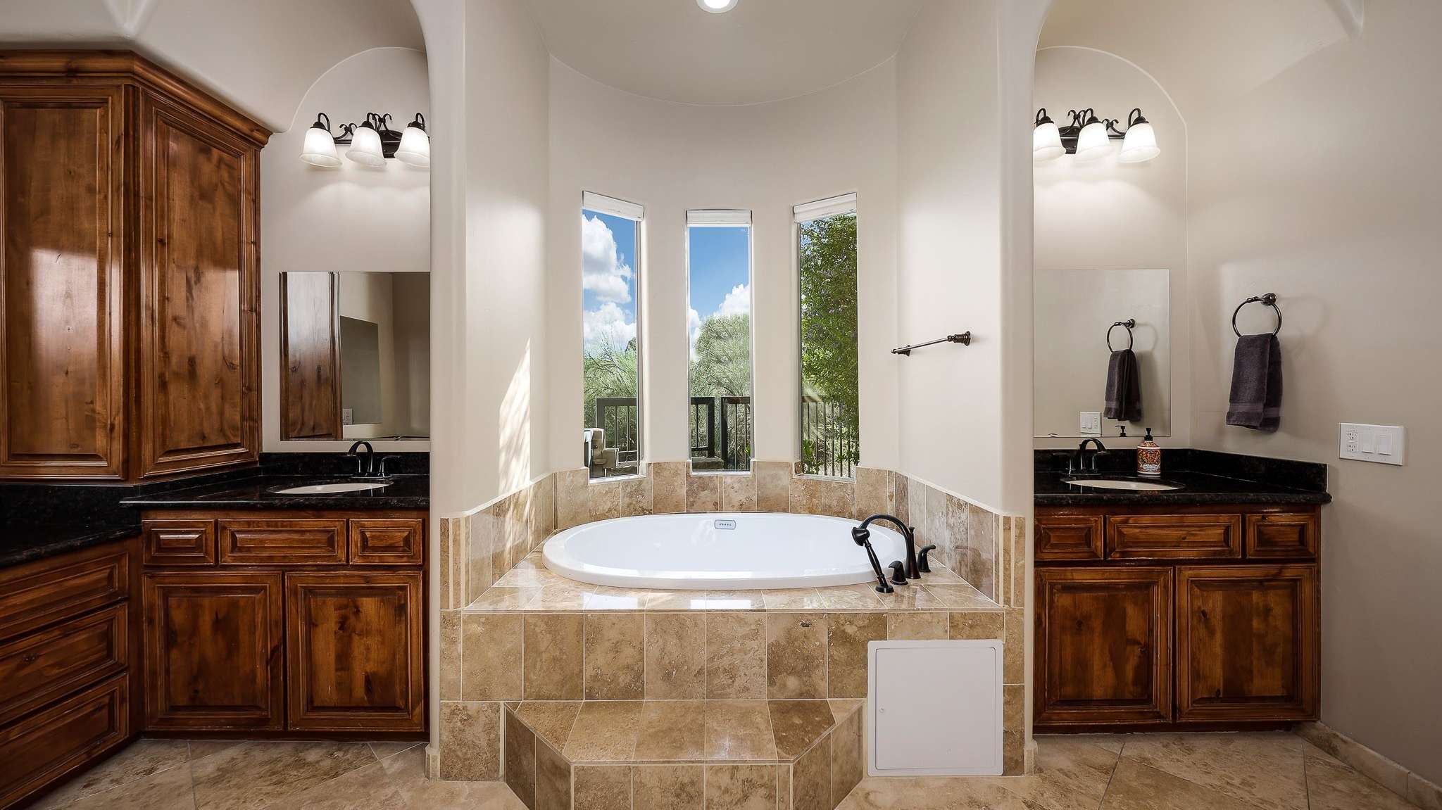 16 of 39. This spa-inspired primary bath offers a deep soaking tub framed by vertical windows and flanked by dual vanities with rich wood cabinetry. A peaceful escape in this beautifully appointed Scottsdale home.