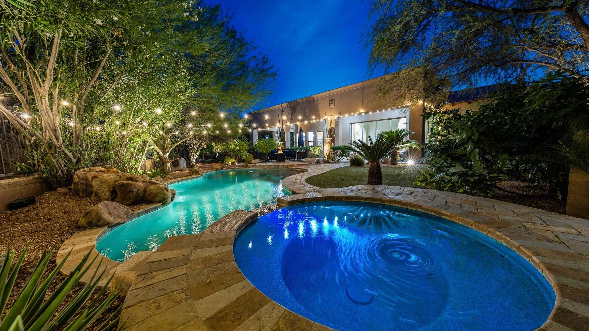 21 of 39. Unwind in this beautifully lit Scottsdale backyard featuring a freeform pool and spa. With lush landscaping, rock accents, and ambient lighting, this outdoor retreat delivers a five-star resort vibe right at home.