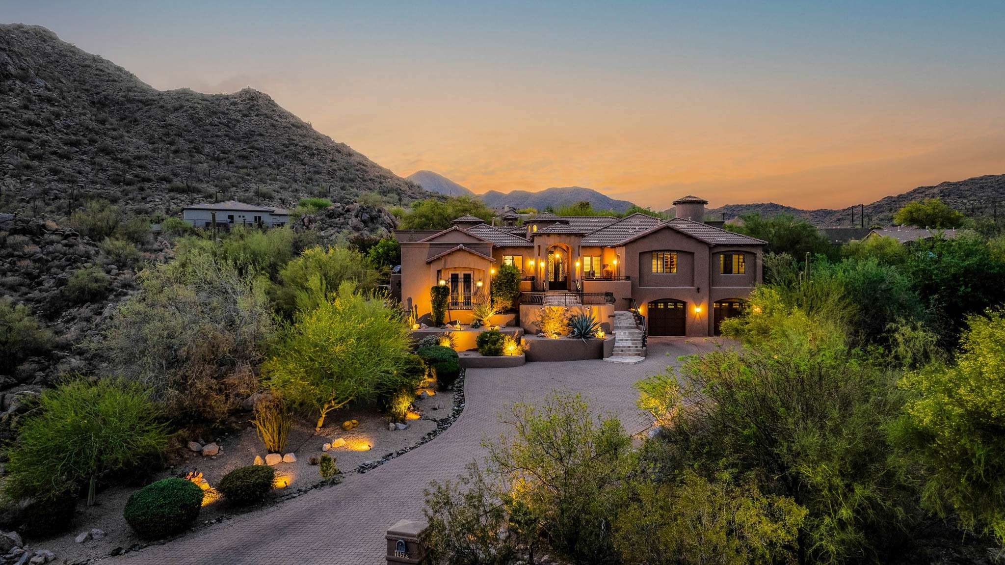37 of 39. This Scottsdale estate makes a bold statement with its elevated position against the backdrop of rugged mountains and soft sunset skies. Surrounded by mature desert flora and enhanced with architectural lighting, the home's striking curb appeal and multi-level design offer a warm welcome to refined desert living.