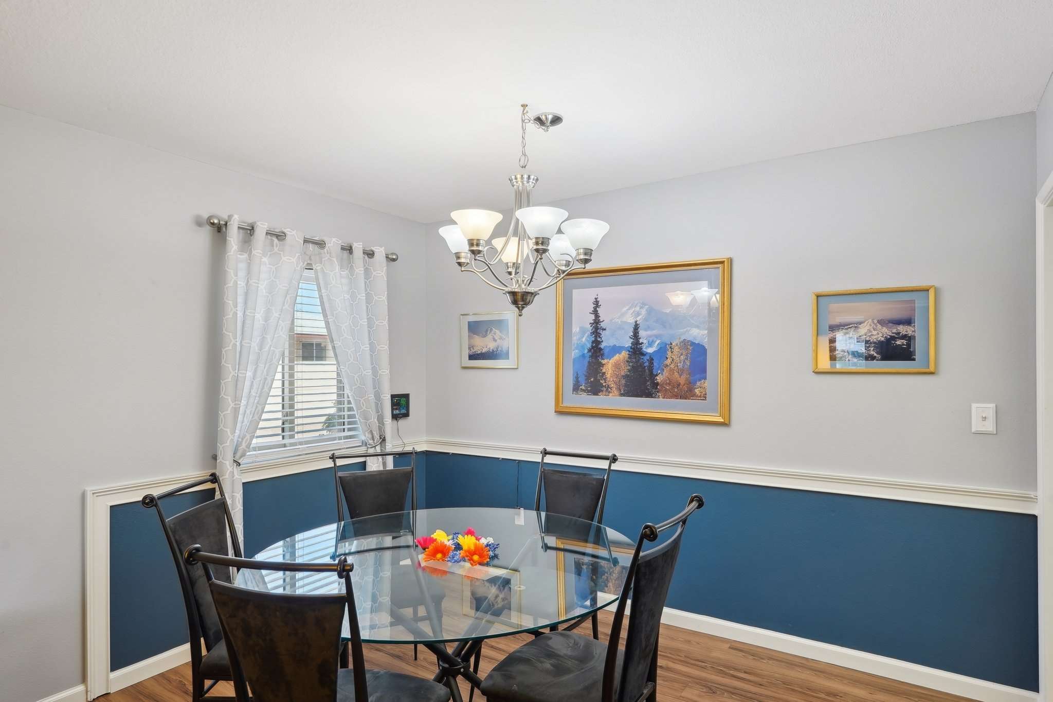 13 of 41. A large window and stylish chandelier highlight this inviting dining space, featuring custom trim details and warm, neutral tones. Ideal for everyday meals or special occasions.