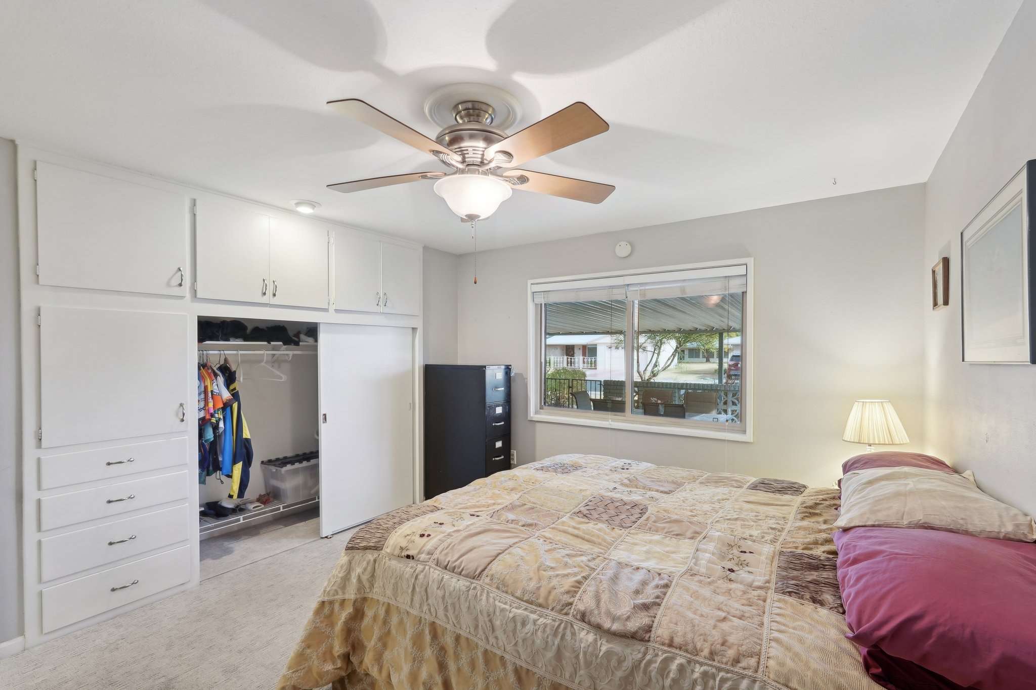 22 of 41. The primary bedroom features ample built-in storage, a ceiling fan, and a large window with patio views. A peaceful retreat with a functional layout.