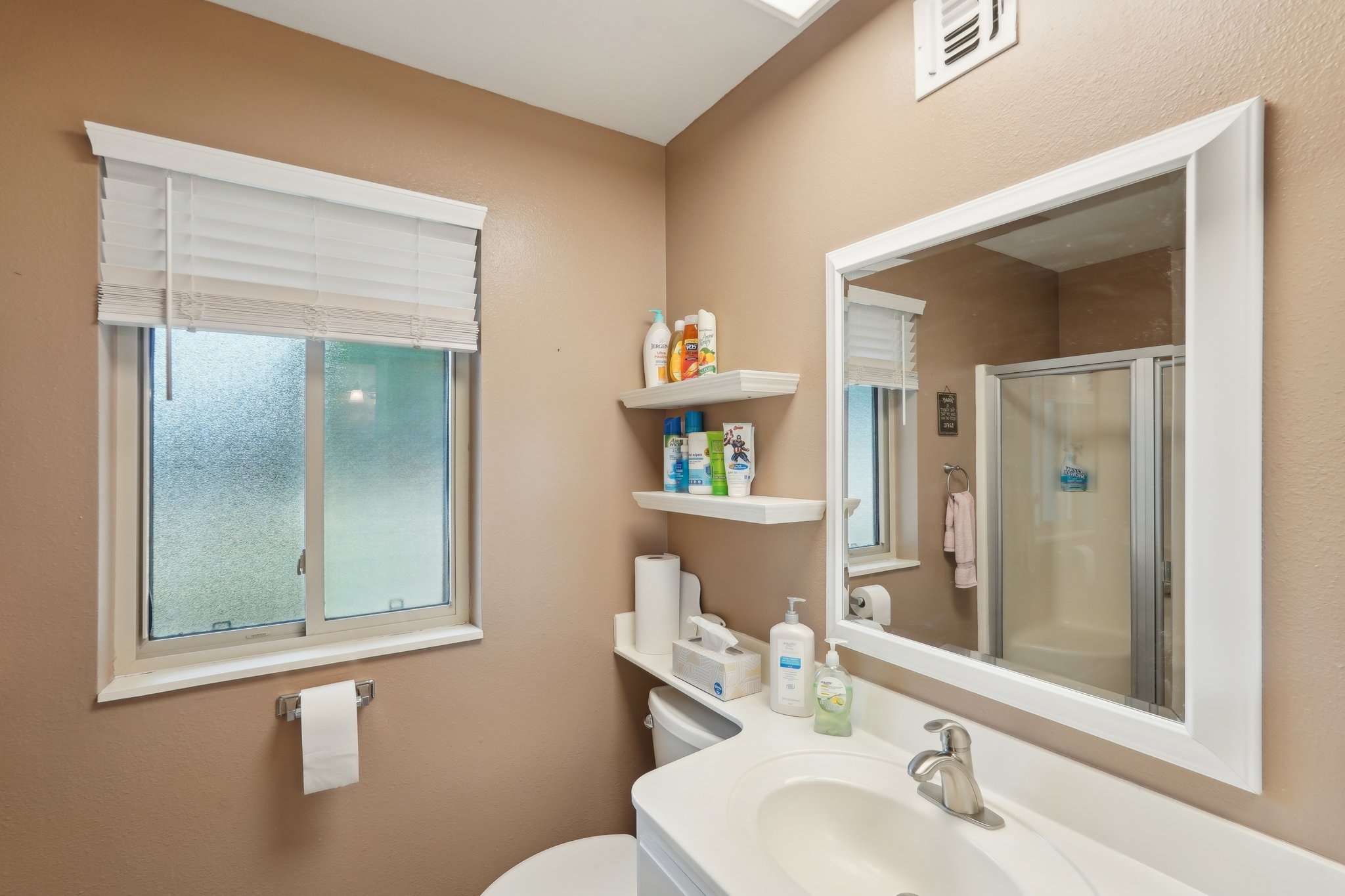 24 of 41. This updated bathroom features a modern walk-in shower with glass doors, built-in shelving, and stylish fixtures. A comfortable and elegant space.