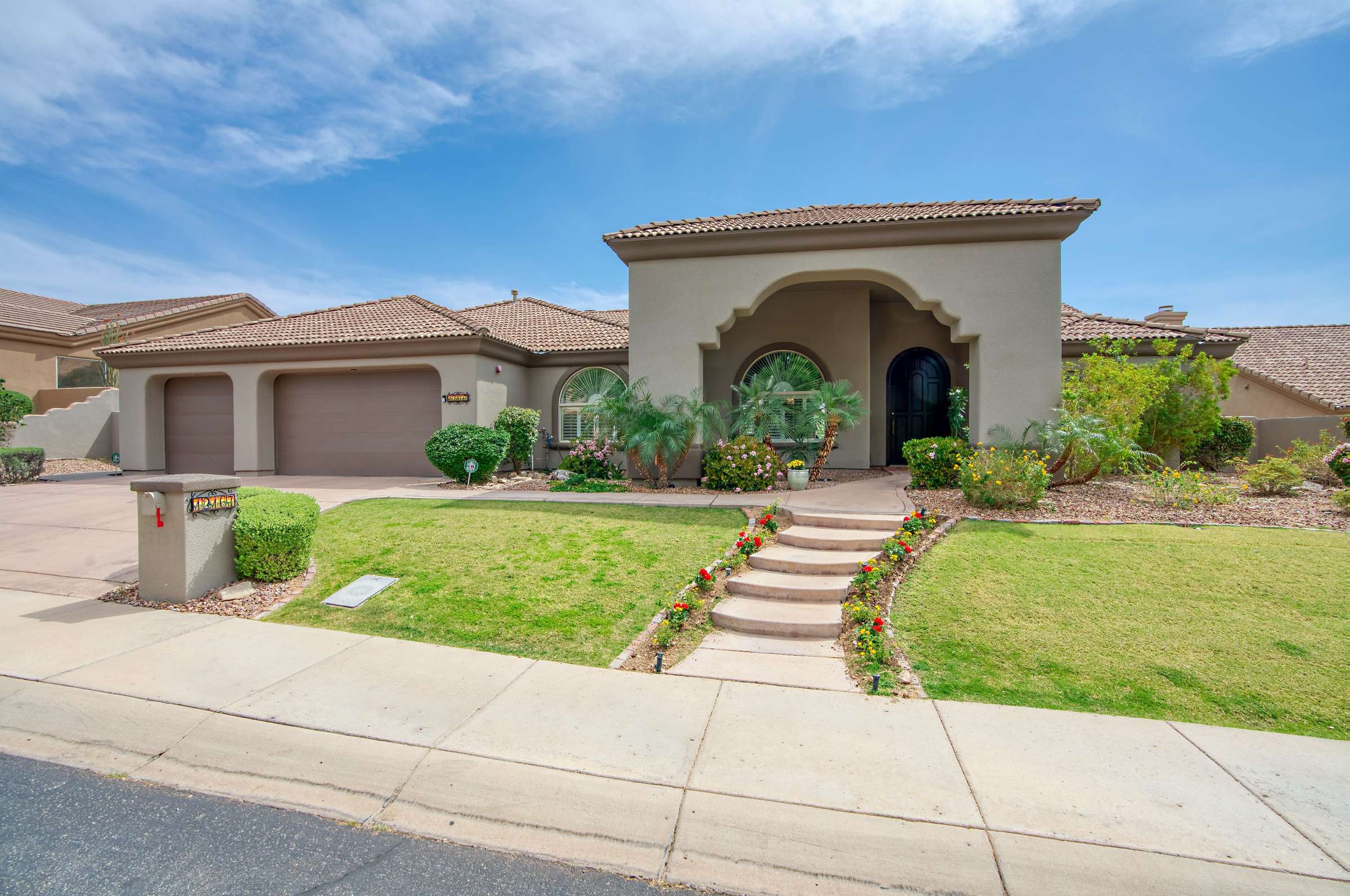 3 of 65. Showcasing arched architecture, a tiled roofline, and triple-car garage, this home stands out in the desirable Sonoran Arroyos. The entry is framed by tropical greenery and updated desert landscaping for a polished, upscale feel.