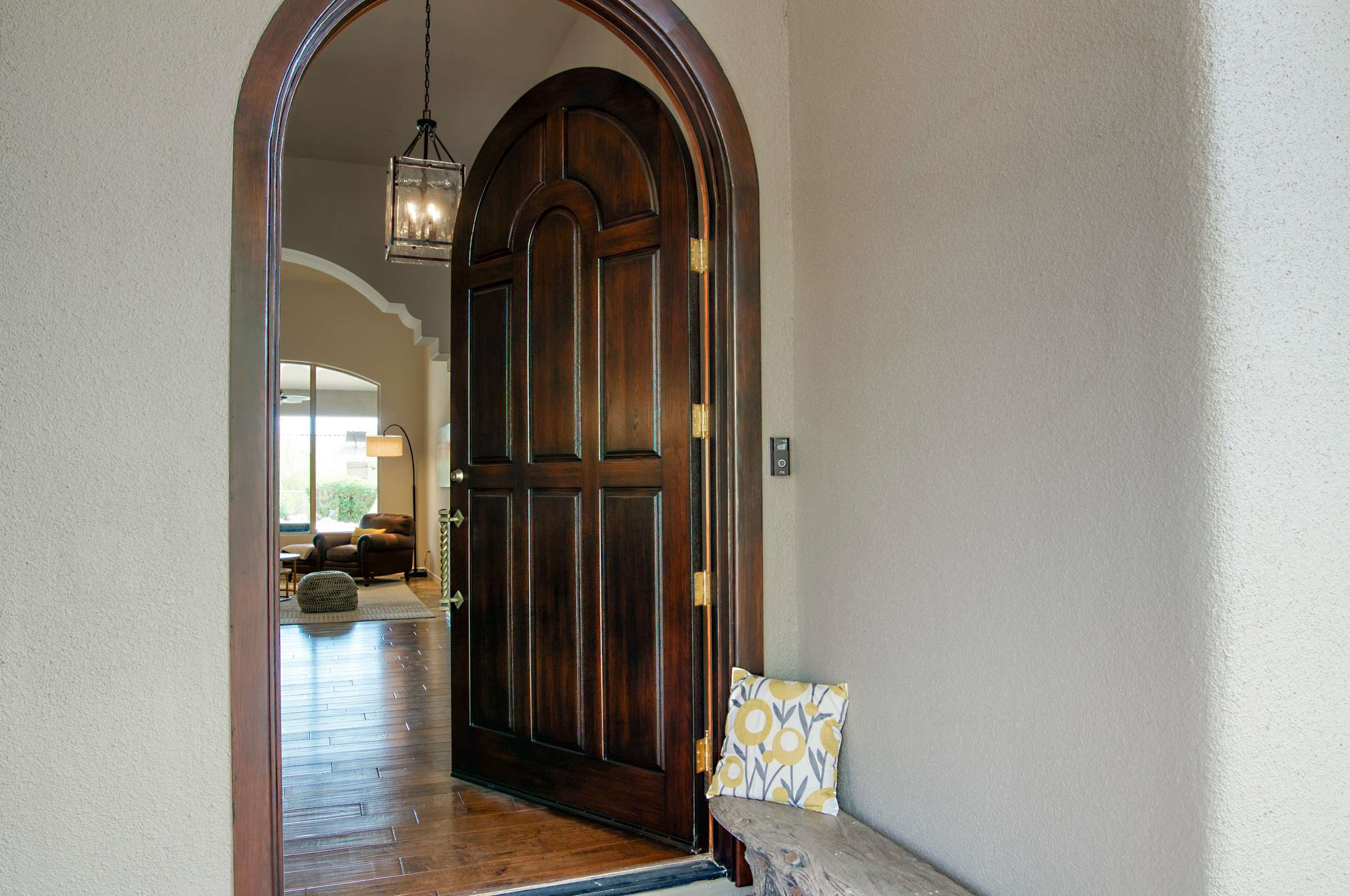 4 of 65. Step into style through a rounded wood door beneath an arched portico. This inviting entryway blends Mediterranean influences with Arizona elegance, setting the tone for the custom design and light-filled interiors found inside.