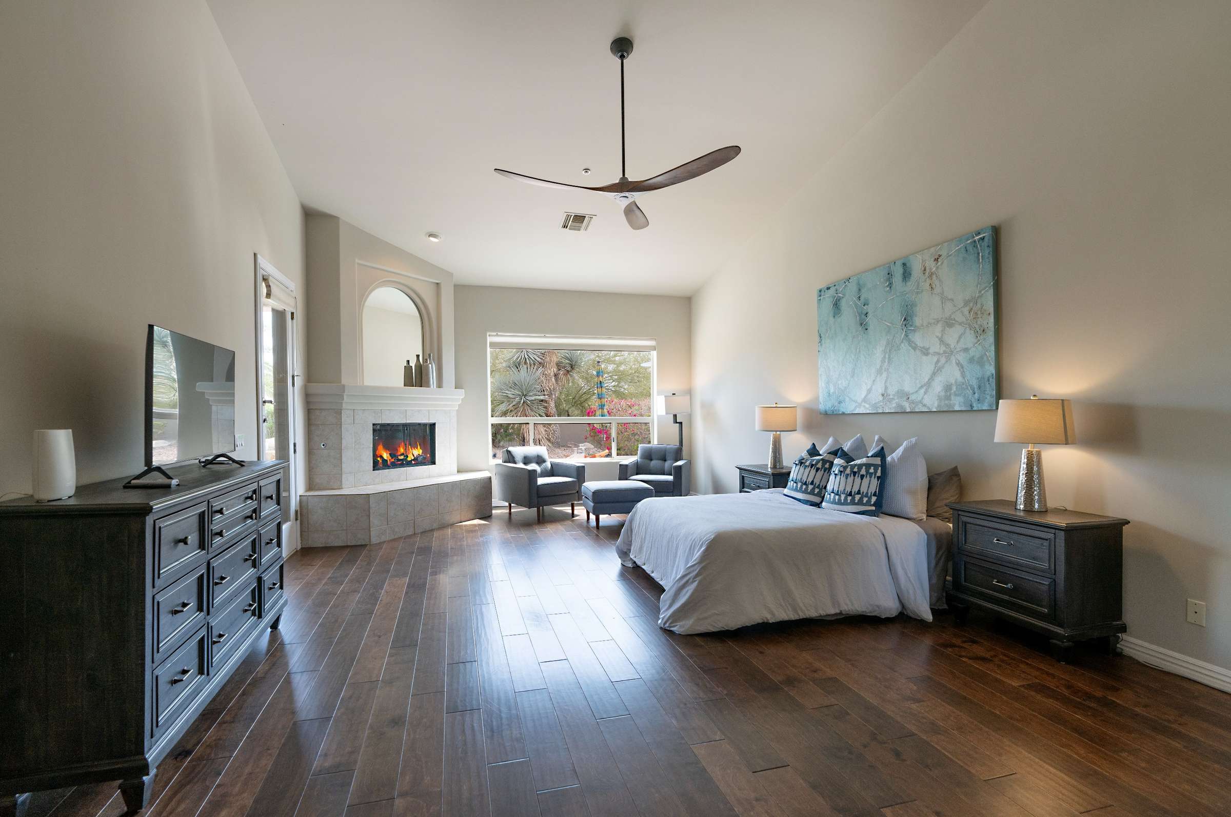 14 of 65. The oversized primary suite features a cozy fireplace, seating area, and rich hardwood floors. Large windows frame desert views, offering both elegance and comfort in this Scottsdale home.