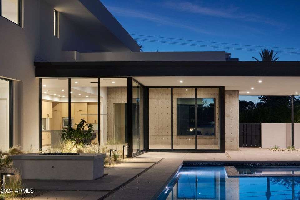 13 of 27. A dramatic detail shot reveals the architectural beauty of the backyard, with glowing reflections on the pool, textured concrete walls, and open-concept living extending outdoors.
